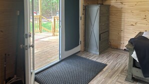Un intérieur en bois avec une porte coulissante donnant sur une terrasse extérieure, un téléviseur fixé au mur et un petit meuble.