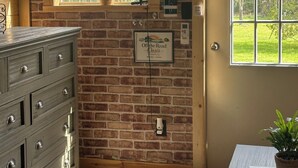 Une pièce avec un mur en briques, une commode en bois, une fenêtre avec une plante, une porte et un panneau accroché au mur.