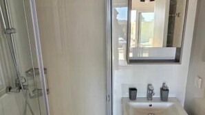 A bathroom with a glass shower enclosure, a sink with a mirror above, and a wooden floor. - Arillas Peaceful Bungalows (Corfu)