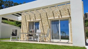 A modern house with a stone facade, large sliding glass doors, and a patio with outdoor furniture. - Arillas Peaceful Bungalows (Corfu)