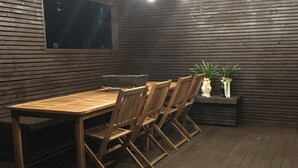 A wooden deck with a dining table and chairs, surrounded by a wooden wall and a window.
