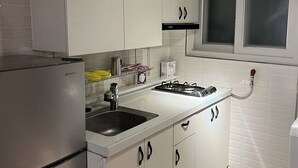 A kitchen with white cabinets, a stainless steel refrigerator, a gas stove, and a window with blinds.