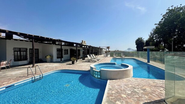 A swimming pool with lounge chairs, a covered seating area, and a view of a mountain.