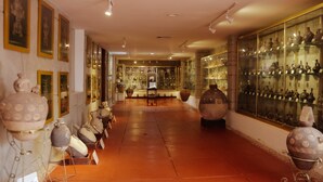 A museum corridor with pottery displays on both sides, a central walkway, and framed pictures on the walls.