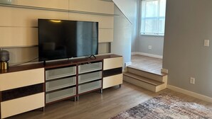 A modern living room with a flat-screen TV, built-in shelving, a staircase, and a large window. - 4-Story Executive - Micro Suite - Private Rooftop - Free Parking (Atlanta)