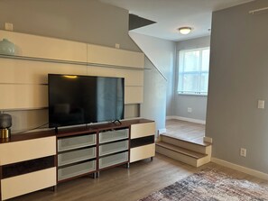 A modern living room with a flat-screen TV, built-in shelving, a staircase, and a large window. - 4 Story Roof Top Loft & Mercedes Stadium View, Walk to FIFA World Cup (Atlanta)