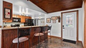 A kitchen with wooden cabinets, a microwave, a refrigerator, and a bar area with stools.