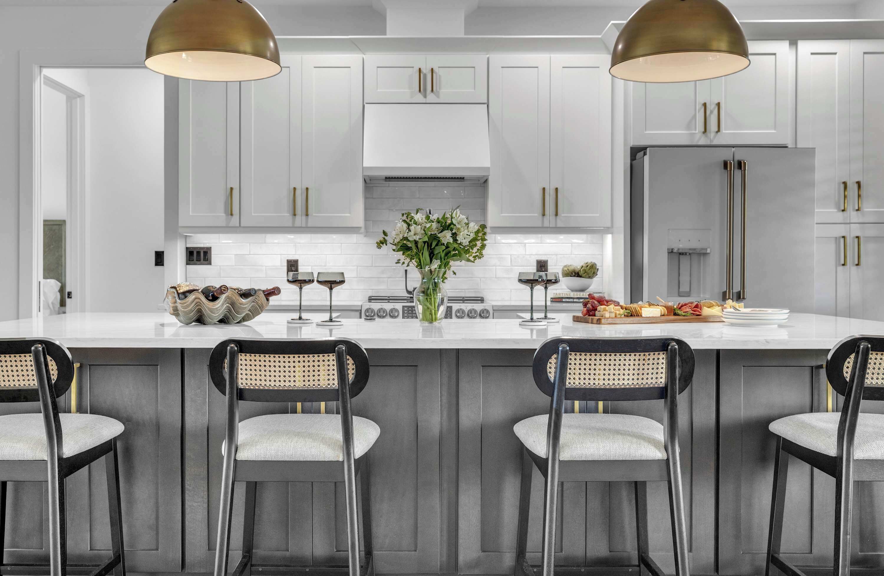A modern kitchen with white cabinets, a central island with bar stools, a stainless steel refrigerator, and pendant lighting.