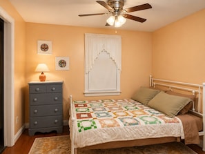 A bedroom with a bed, a dresser, a ceiling fan, and a window with a white valance.