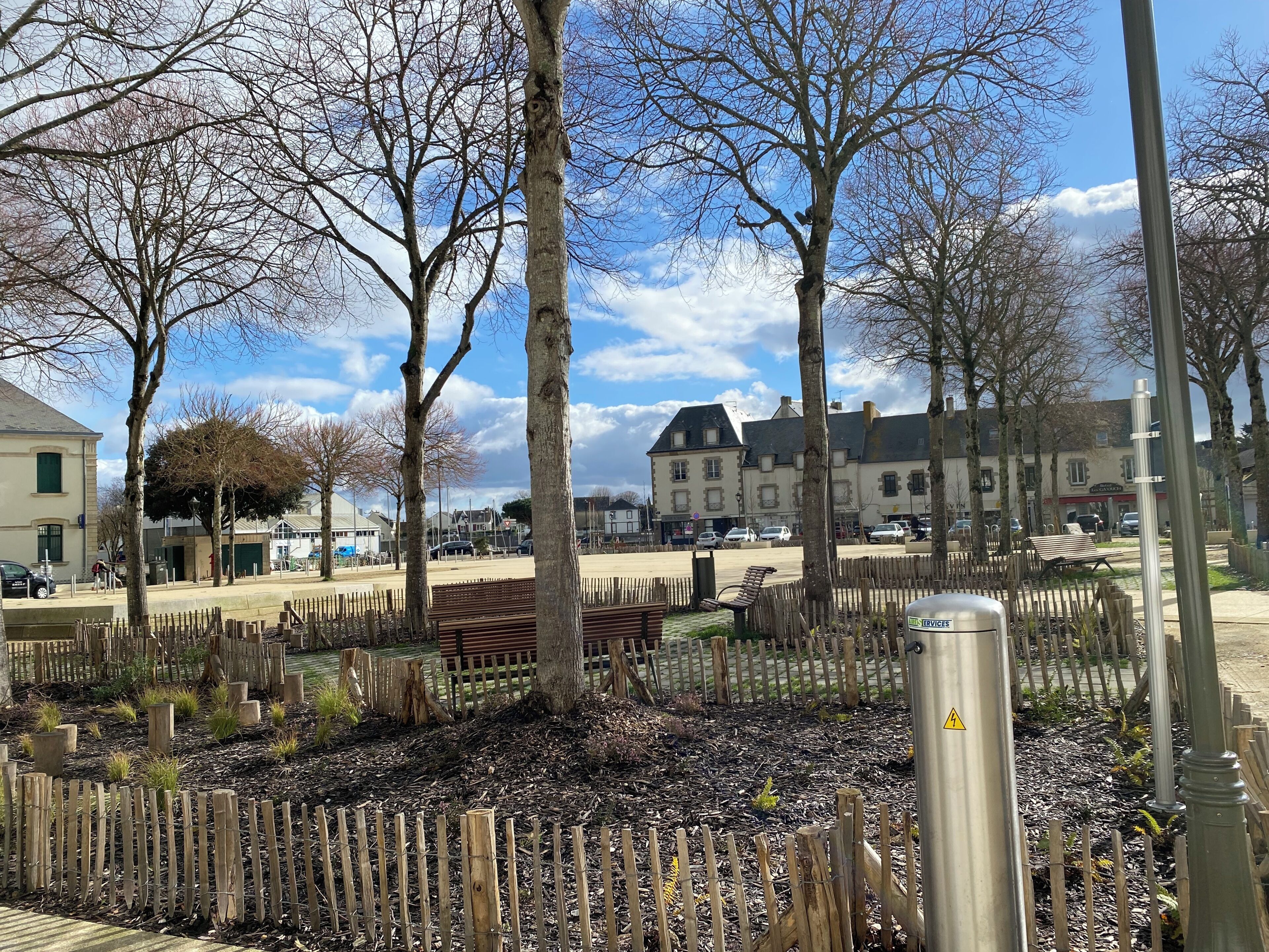 Un parc avec des bancs, des arbres et un bâtiment en arrière-plan.