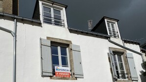 Un bâtiment blanc avec une grande porte en arc de cercle, une petite fenêtre et une enseigne indiquant qu’il y a des articles en vente.