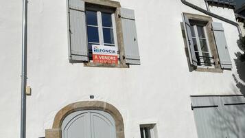 Un bâtiment blanc avec une grande porte en arc de cercle, une petite fenêtre et une enseigne indiquant qu’il y a des articles en vente.