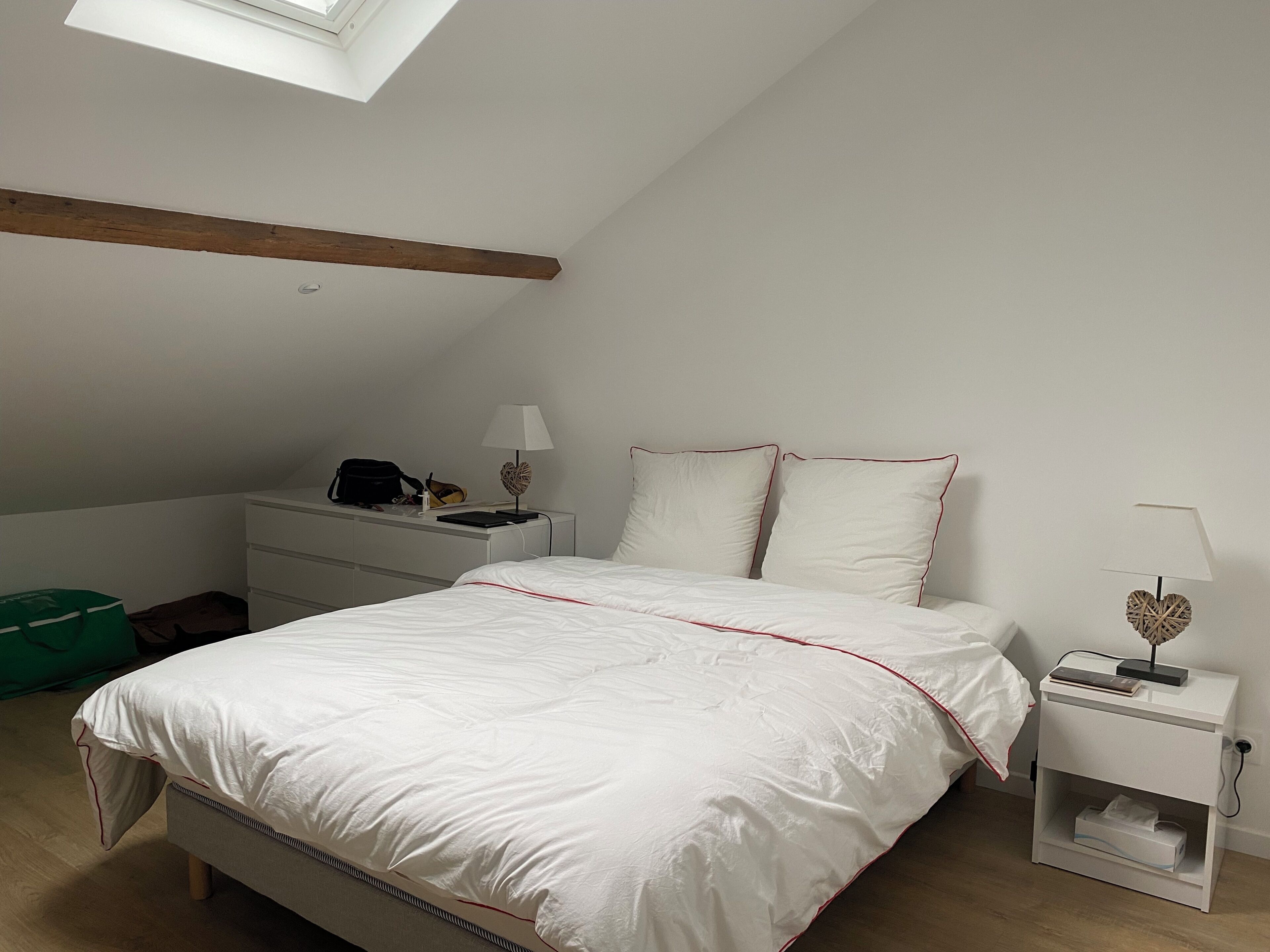 Une chambre à coucher avec un lit, des tables de chevet, un bureau et un sac vert.