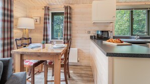 Interior em madeira com uma mesa de jantar, cadeiras, uma lâmpada, micro-ondas e janela com cortinas.