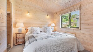 Quarto com painéis de madeira, uma cama, duas luminárias de cabeceira, uma janela e uma mesa de cabeceira.