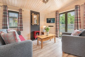 A cozy living room with a wooden ceiling, a flat-screen TV, a red stove, and grey sofas.