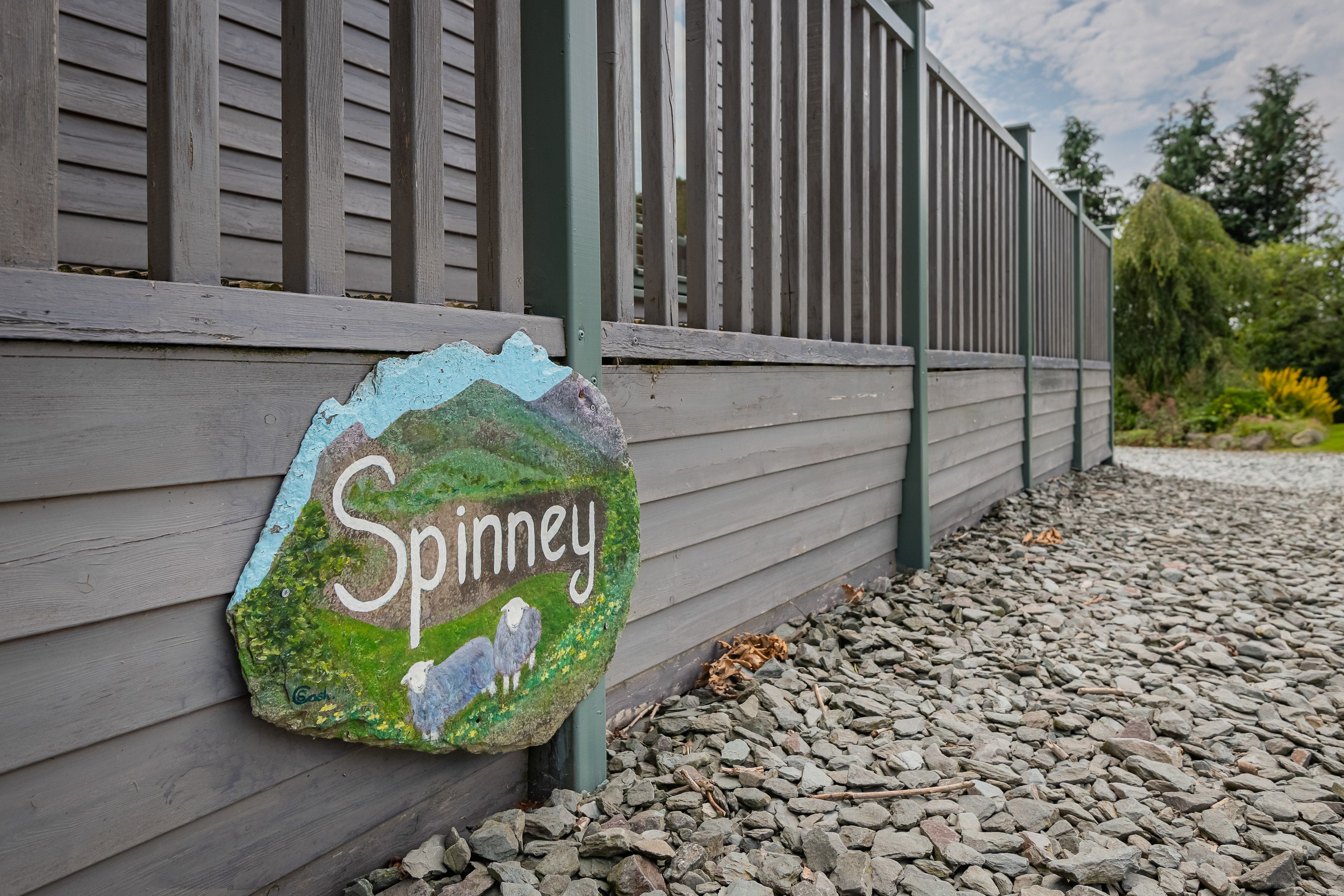 Une vieille enseigne, portant le nom « Spinney » et une illustration de mouton, est fixée à une clôture en bois.