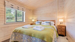 Een slaapkamer met houten lambrisering, een bed, twee nachtkastjes, een raam met zonwering en een lamp op elk kastje.