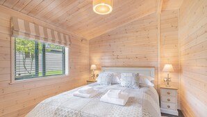 Une chambre à coucher aux murs lambrés, avec un lit, deux tables de chevet dotées de lampes et une fenêtre avec des stores.