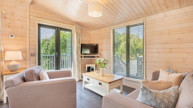 L’intérieur d’un chalet en bois, avec un canapé, une table basse, un téléviseur et de grandes fenêtres.
