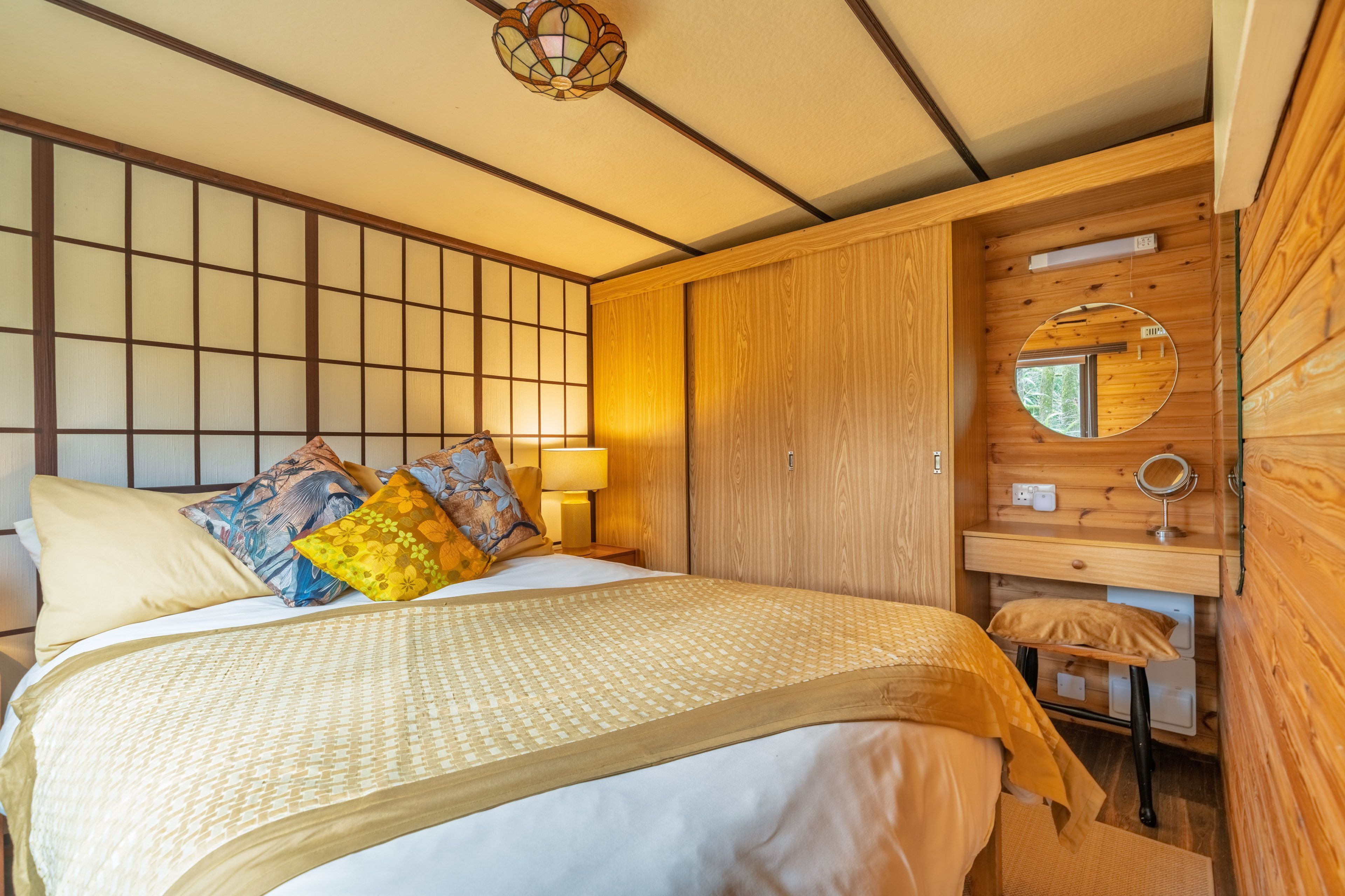 A traditional Japanese-style bedroom with tatami flooring, a low wooden bed, a shoji screen, and a small wooden desk with a mirror.