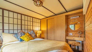 A traditional Japanese-style bedroom with tatami flooring, a low wooden bed, a shoji screen, and a small wooden desk with a mirror.