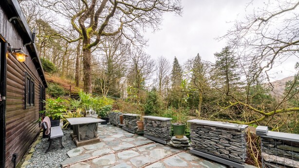 A stone patio with a table and chairs, surrounded by potted plants and a stone wall.