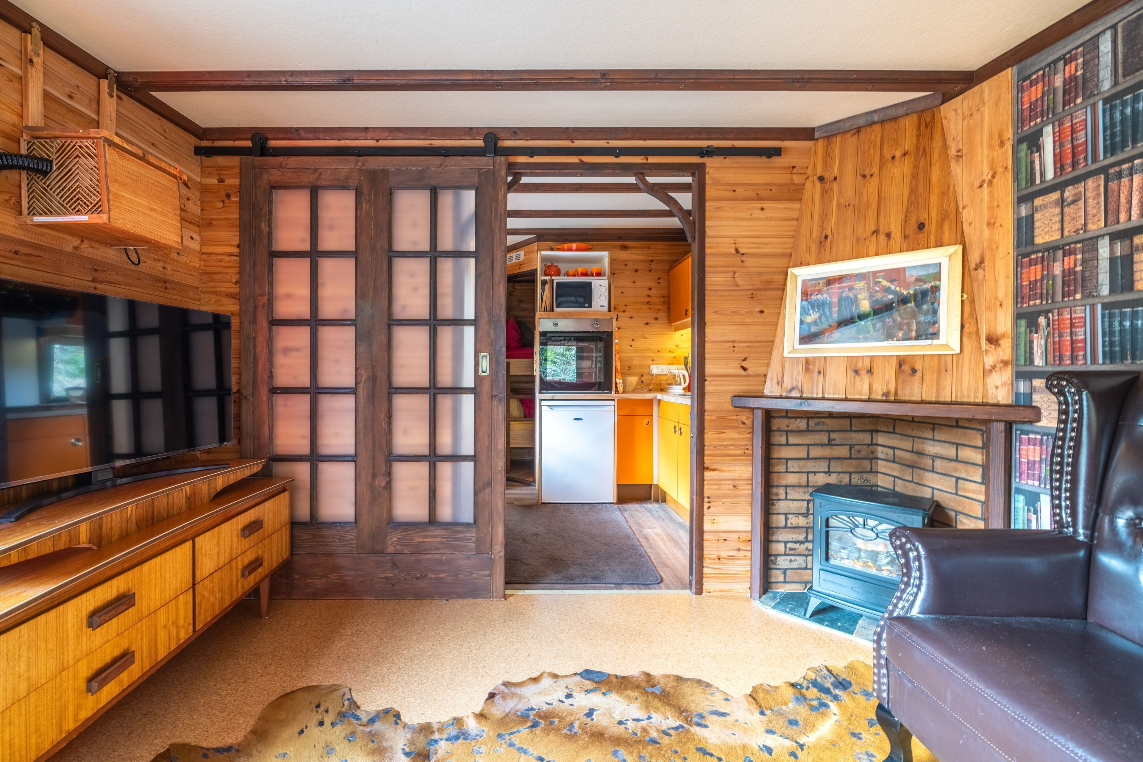A wooden interior with a television, a fireplace, and a kitchen area.