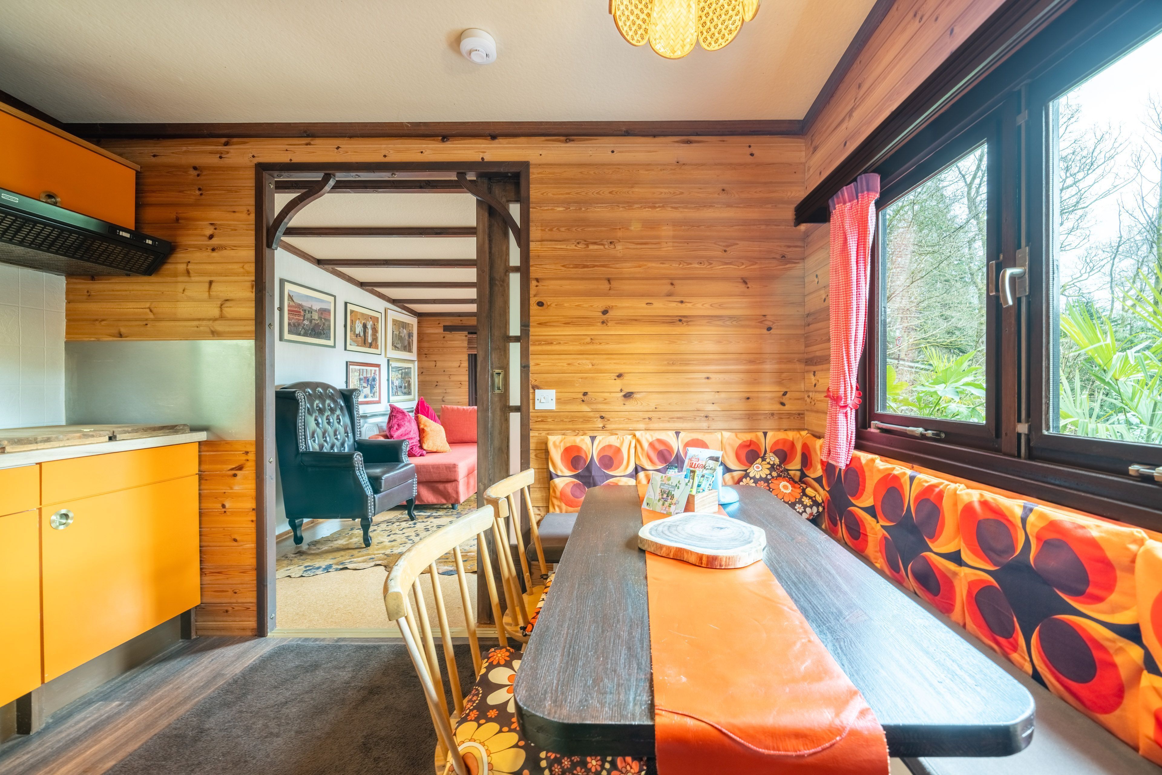 A wooden interior with a dining table, chairs, a bench, and a window with curtains.