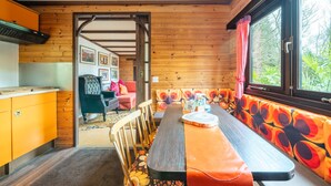 A wooden interior with a dining table, chairs, a bench, and a window with curtains.
