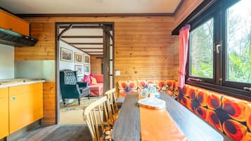 A wooden interior with a dining table, chairs, a bench, and a window with curtains.
