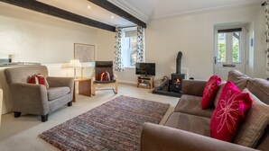 A living room with a sofa, armchair, TV, fireplace, and a window with curtains. - Ben Place Cottage -  A short stroll from Grasmere Village (Grasmere)