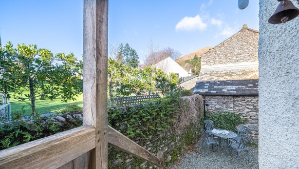 A wooden deck with a stone wall, outdoor seating, and a view of a building with a stone roof. - Ben Place Cottage -  A short stroll from Grasmere Village (Grasmere)