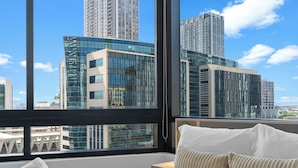 Een hotelkamer met een groot raam, een bed met witte lakens en uitzicht op hoge gebouwen.