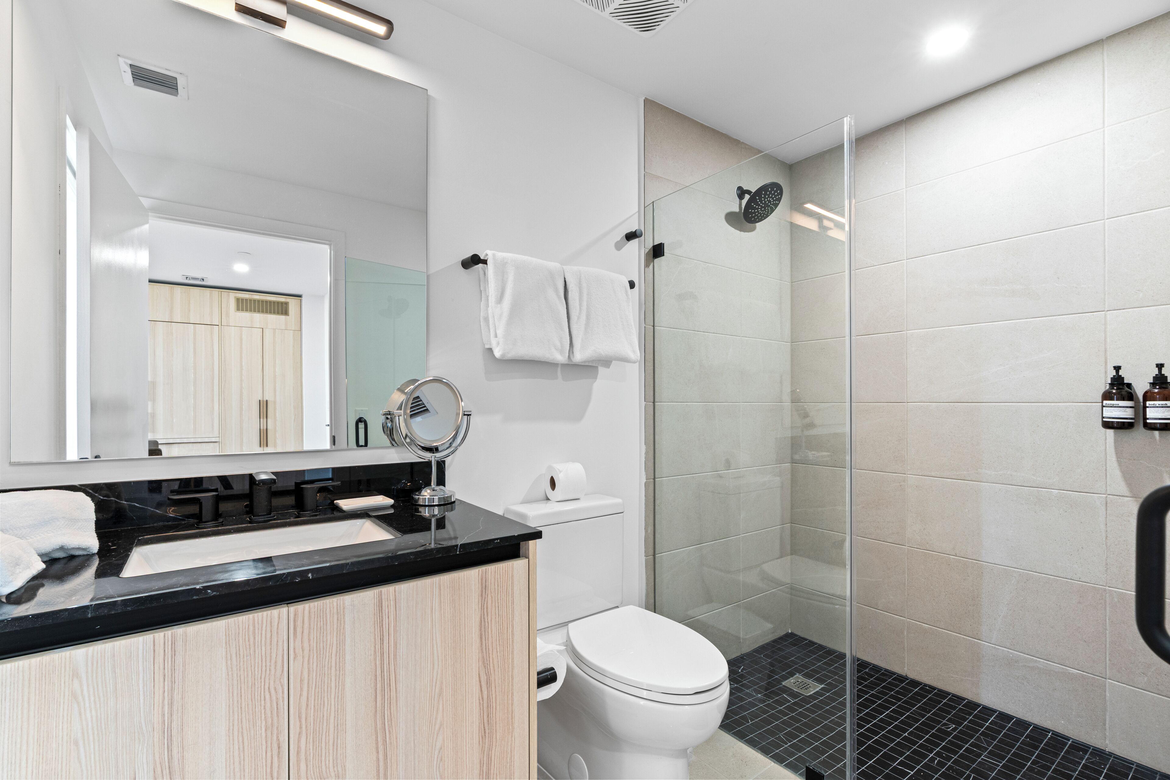 Een moderne badkamer met een zwart aanrecht, een wit toilet en een douchecabine met glazen wanden.