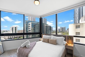 A modern hotel room with a large bed, two bedside tables, a nightstand, and a view of the cityscape through large windows. - District 225 (Miami)