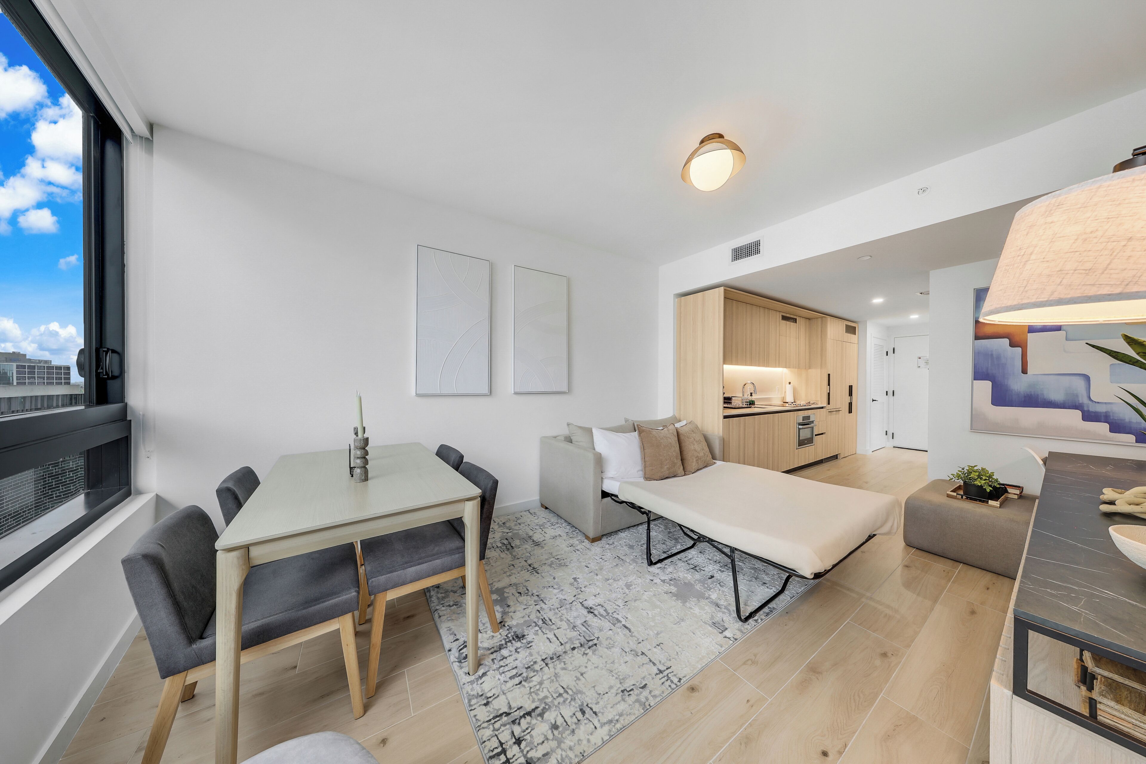 En modern lägenhet med matplats, soffa, litet kök och ett stort fönster.