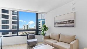 Een moderne woonkamer met een groot raam, een bank, een fauteuil, een salontafel en een plant.