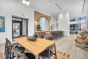 Een modern interieur met een houten eettafel, zwarte stoelen, een bar en een zithoek met sofa's en fauteuils.
