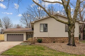 A single-story house with a garage, a small front yard, and a tree in front.