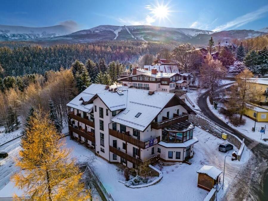 A multi-story hotel with a ski lift in the background, surrounded by snow-covered trees and mountains.