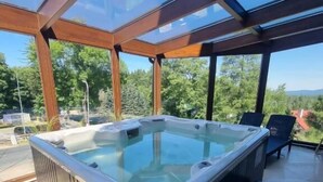 A hot tub in a glass-enclosed patio area with chairs and a view of trees and mountains. - Karpacki&SPA z Restauracją  (Karpacz)