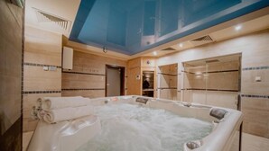 A hot tub in a room with tiled walls, a ceiling with a blue tint, and a door leading to another room. - Karpacki&SPA z Restauracją  (Karpacz)