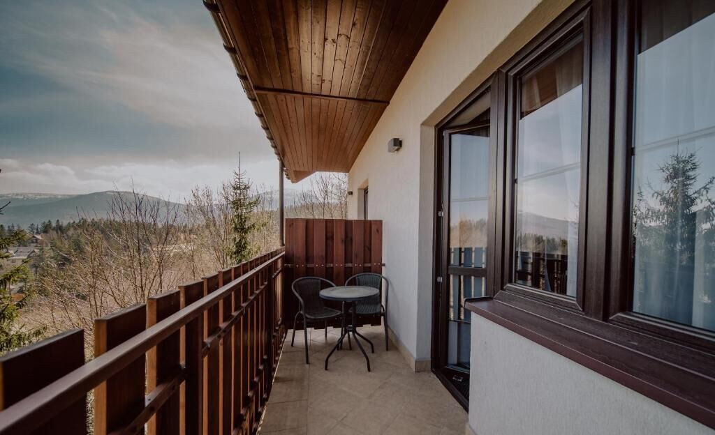 A balcony with a wooden railing, two chairs, and a table.