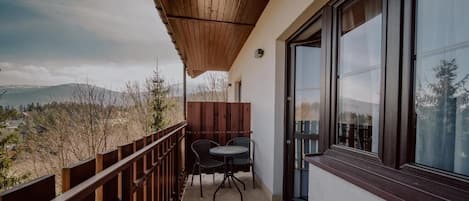 A balcony with a wooden railing, two chairs, and a table.
