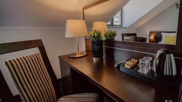 Une chambre d’hôtel avec un bureau en bois, une lampe, une plante en pot, une bouilloire et un plateau contenant un livre et des verres.