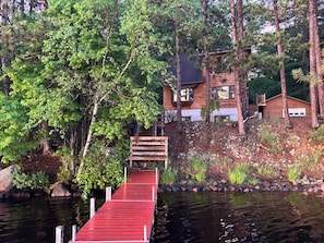 A wooden dock leading to a house surrounded by trees. - Charming 3-bedroom lake house in Rhinelander perfect for your getaway (Rhinelander)