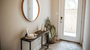 A hallway with a wooden console table, a round mirror, a potted plant, and a door leading to an outdoor area. - Stay in the Heart of Houston, 5' to Downtown, close Medical Center & World Cup (Houston)