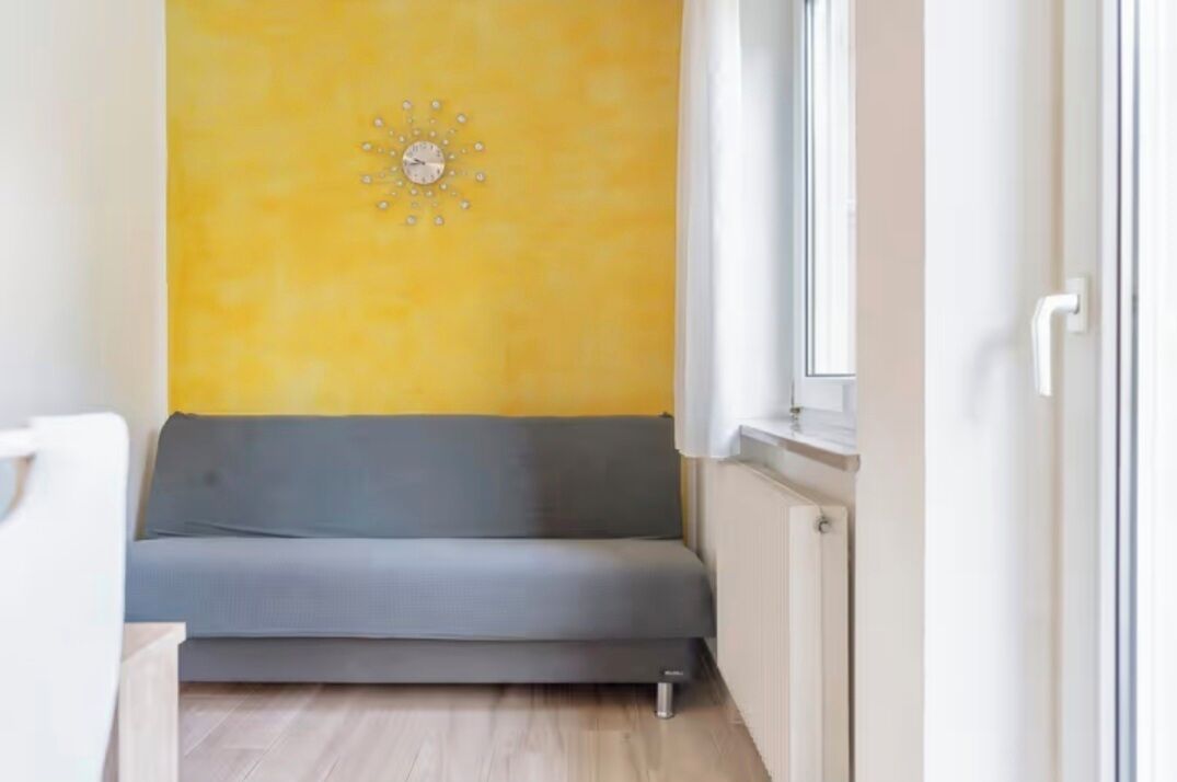 A room with a grey sofa, a yellow wall, and a window.