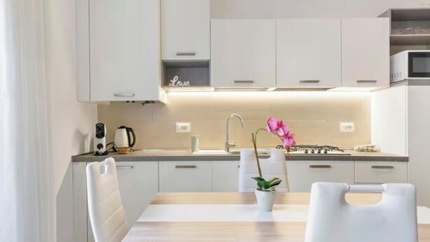 Eine moderne Küche mit weißen Schränken, einem Holztisch und einer rosa Orchidee.